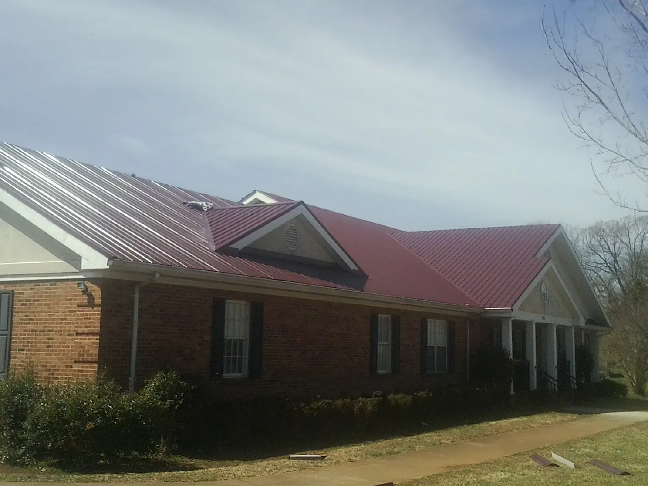 Red metal roof with gabled entries on a long brick building, from a Hail Damage Roof Repair job in Highland